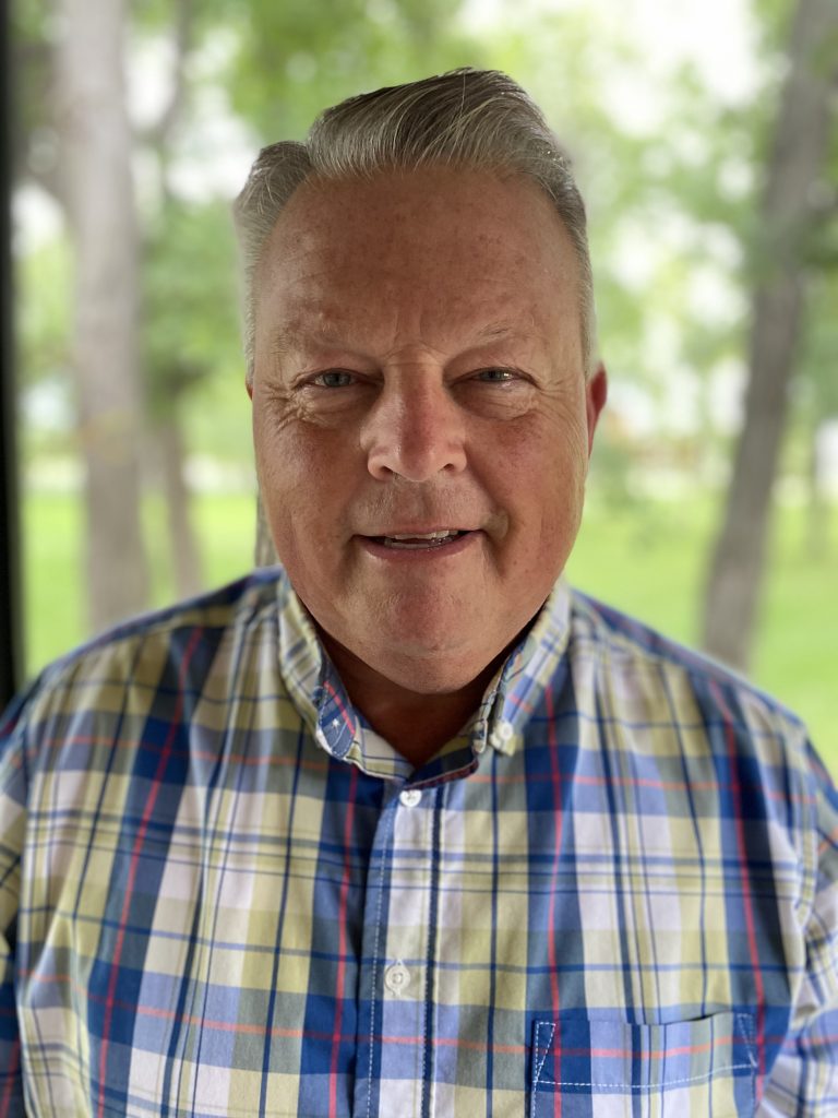 Man in a checkered shirt with grey hair smiling