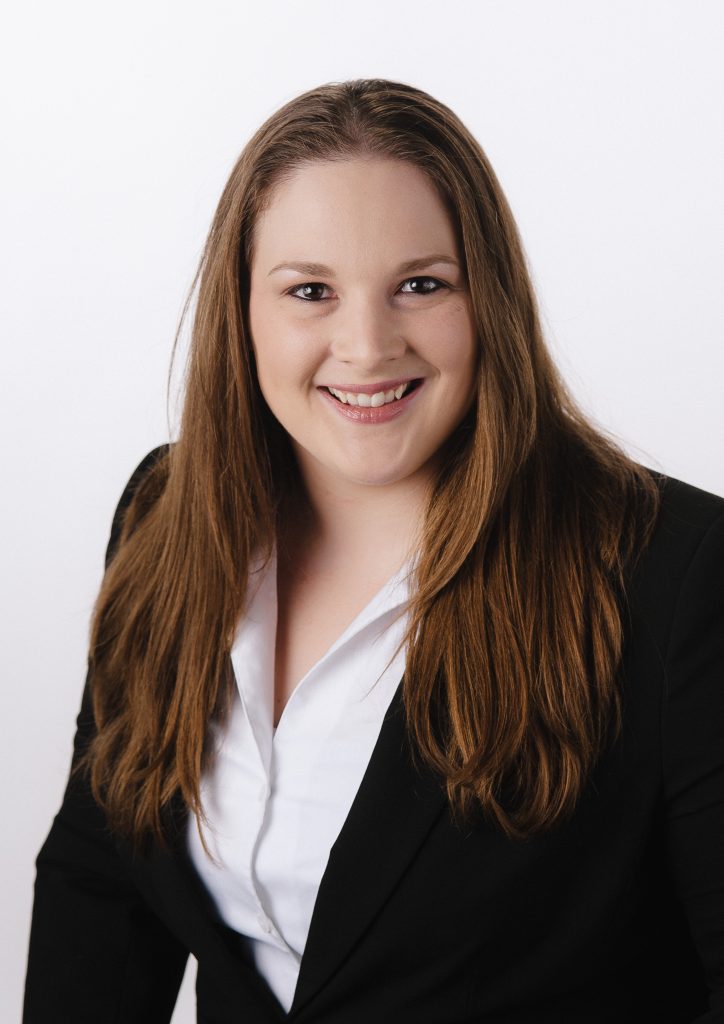 Woman with long brown hair in a white button up shirt and black suit coat smiling