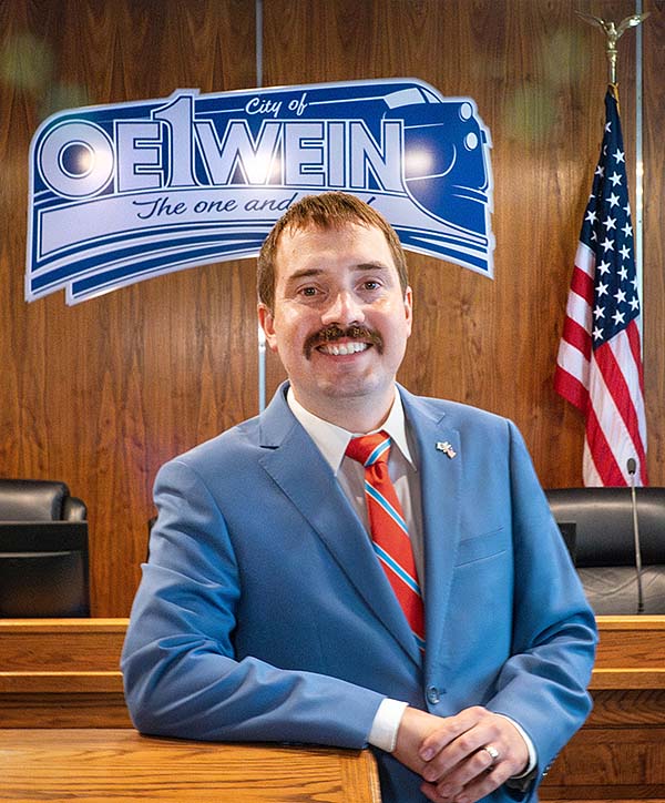 Man with a mustache in a blue suit and red tie smiling