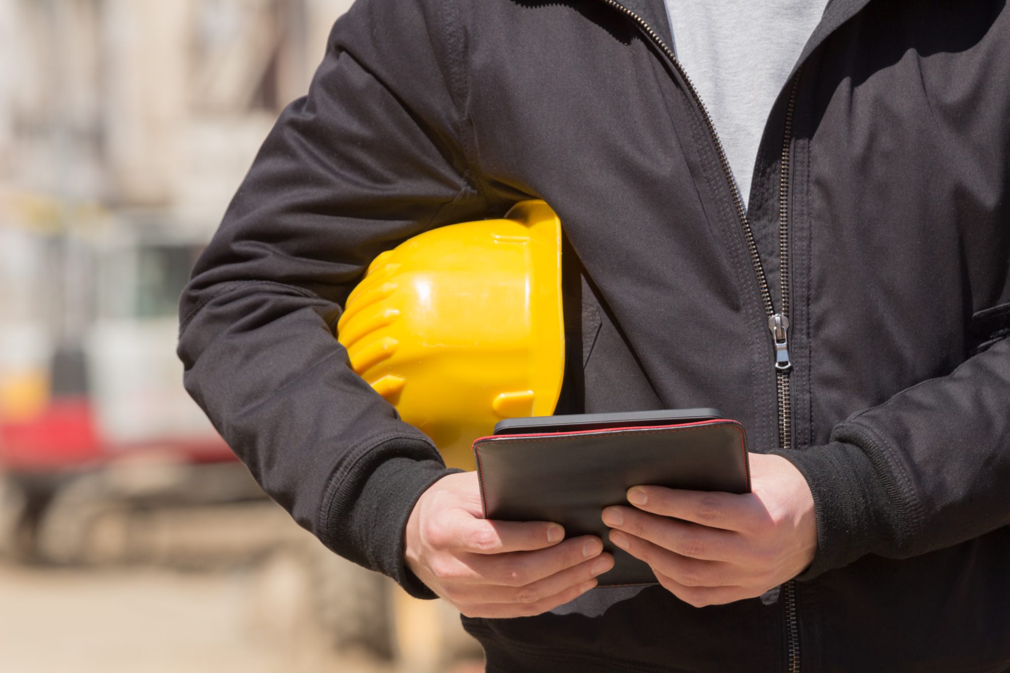 Construction engineer making notes on a tablet and holding a yellow hard hat