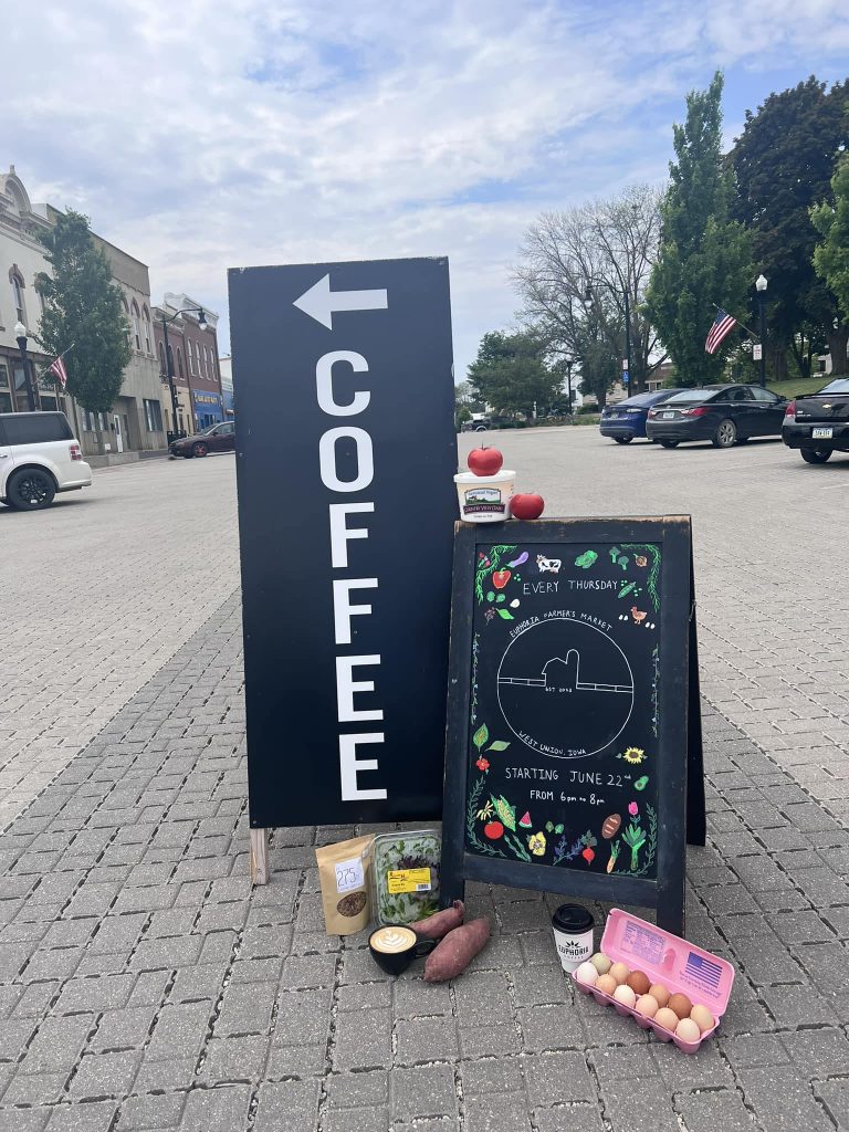 Sign that says Coffee next to a farmers market sign in a downtown street