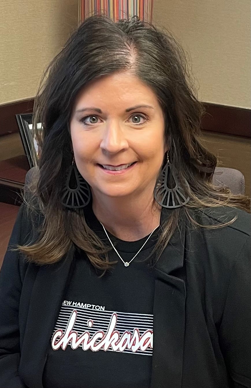 Woman in t-shirt and black blazer smiling.