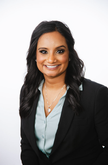 Woman in light blue button up shirt and black blazer smiling.